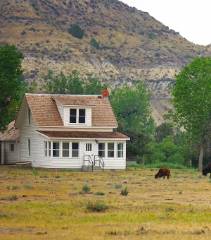 A brown and white house near mountains with animals grazing