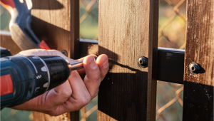 Someone using a drill to install a wooden fence