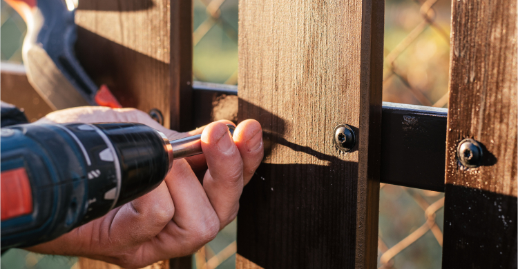 Someone using a drill to install a wooden fence